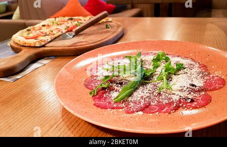 Carpaccio de bœuf, filet de bœuf, courgettes, câpres, pizza au pepperoni servie sur une table dans un restaurant italien. Banque D'Images