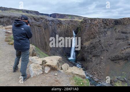 Visiteur prenant la photo de la magnifique cascade de Litlanesfoss où l'eau tombe entre la géologie massive de la colonne de basalte, Islande. Banque D'Images