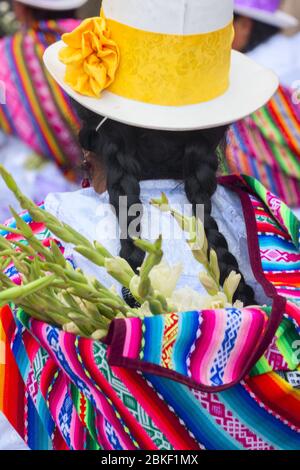 Une femme péruvienne avec les longs tresses de cheveux noirs, portant des vêtements traditionnels colorés et un chapeau melon brun en feutre marchant dans les rues de Cusco Banque D'Images
