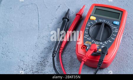 Multimètre rouge ou multitesteur, également appelé VOM sur une table grise. Instrument de mesure électronique. Fils rouge et noir Banque D'Images