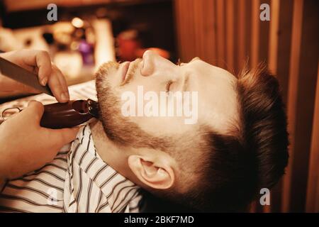 Barber ravira sa barbe à l'homme hippster dans le barbershop. Photo aux tons, style vintage. Banque D'Images