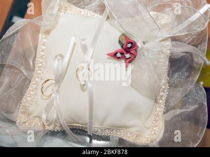 Deux anneaux dorés attachés avec des noeuds à un petit coussin blanc avec des fleurs rouges. Banque D'Images