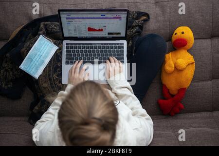 Toronto, Canada - mai 2,2020 : vue de dessus d'une femme assise sur un canapé à l'aide d'un ordinateur portable, avec masque facial et jouet en peluche. Travaillez à domicile sur le coronavirus qua Banque D'Images