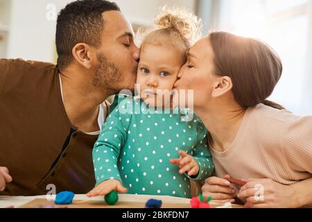 Les parents adorants embrassent leur petite fille mignonne dans les joues, la poitrine horizontale relevée tir Banque D'Images