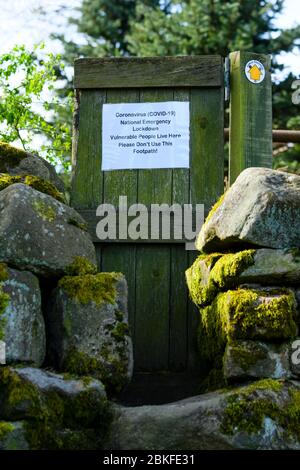 Avis non officiel de demande sur une porte en bois par un panneau public de sentier (flèche jaune à droite) pendant le verrouillage du coronavirus - Yorkshire Angleterre Royaume-Uni Banque D'Images