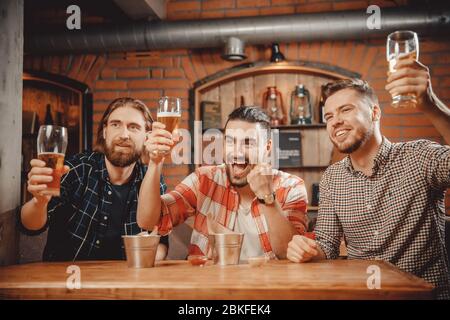 Les fans sont heureux de leur score. Bière pour boisson de style décontracté. Verres relevés au pub montrant la traduction en direct du match Banque D'Images