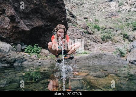 jeune randonneur qui boit de l'eau de ruisseau en montagne Banque D'Images