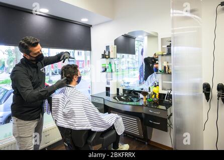 Mayence, Allemagne. 04 mai 2020. Un coiffeur coupe les cheveux d'un client dans le "barbershop" dans le centre ville, protégé par un mur de séparation. La boutique du salon de coiffure est complètement réservée, les clients font la queue devant la boutique. Les terrains de jeux pour enfants et les équipements d'entraînement en plein air sont de nouveau ouverts, les coiffeurs sont autorisés à couper les cheveux à nouveau. Mais des règles d'hygiène strictes sont toujours applicables. Crédit: Andreas Arnold/dpa/Alay Live News Banque D'Images