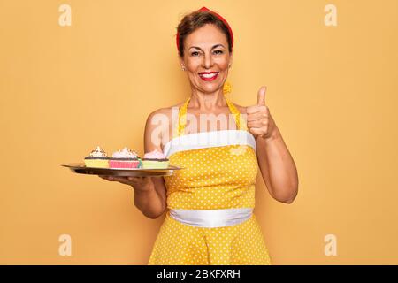 Femme âgée de taille moyenne avec robe rétro de style 50 ans, avec placards heureux avec grand sourire, signe ok, pouce vers le haut avec les doigts, exc Banque D'Images