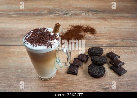 Cappuccino dans une tasse de verre avec biscuits bruns et morceaux de chocolat sur bois brun. Banque D'Images