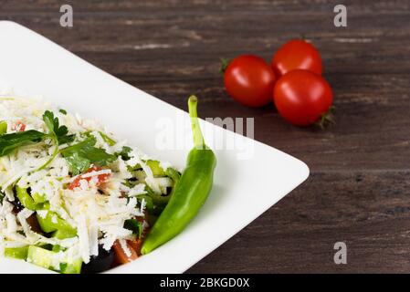 Salade traditionnelle classique Shopska avec tomates, poivrons, concombres et fromage dans un plat blanc sur une table en bois gris. Cuisine bulgare, culture balkanique Banque D'Images