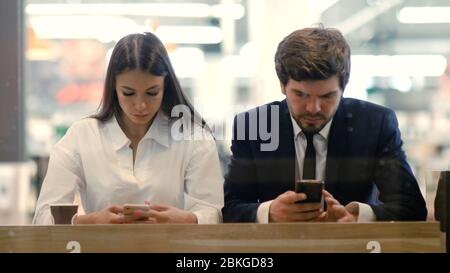 Homme et femme assis dans le café du centre commercial en utilisant leur smartphone. Banque D'Images