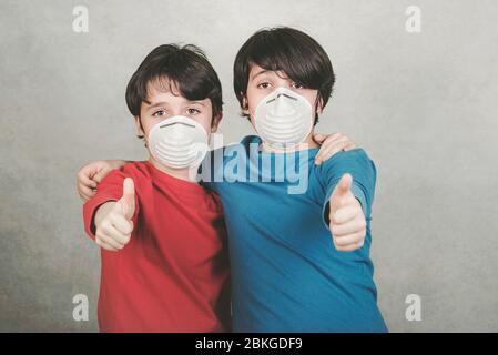 Coronavirus.deux enfants avec masque de visage montrant le pouce vers le haut sur fond gris Banque D'Images