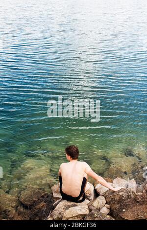 Un homme nage dans l'eau cristalline d'un lac avec une rive rocheuse Banque D'Images