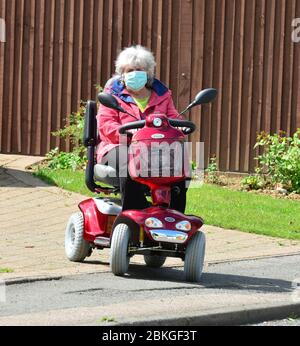 Une Dame sur un scooter mobile portant des EPI pendant le verrouillage du système Covid-19 Banque D'Images