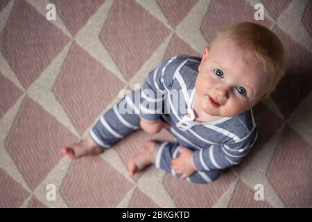 Un petit garçon mignon s'est assis sur un étage de pépinière qui regarde l'appareil photo Banque D'Images