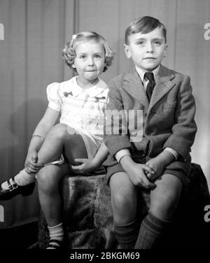 Deux enfants charmants posent dans un studio de photographe dans leurs meilleurs vêtements, pris au début des années 1950 Banque D'Images