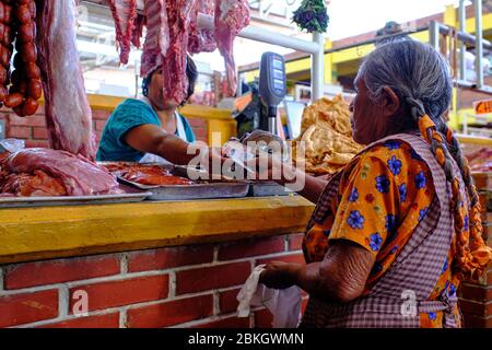 Vieille dame autochtone avec des tresses payant avec de l'argent pour la viande qu'elle a achetée dans un boucher dans le marché de Zaachila. Banque D'Images