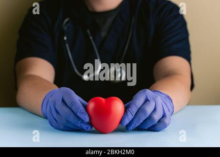 Un professionnel de la santé avec des mains gantées tenant un coeur lu Banque D'Images