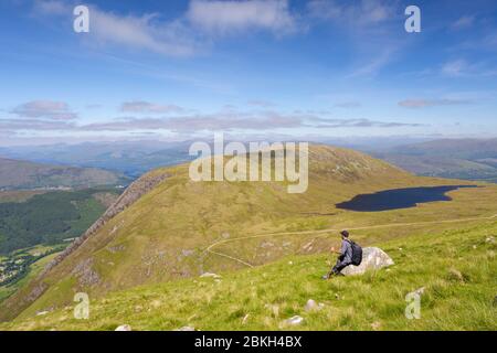 Un randonneur assis sur un rocher en admirant la vue sur Ben Nevis, Scottish Highlands, Écosse Banque D'Images