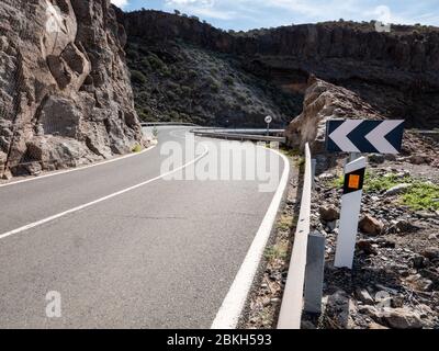 Route sinueuse devant vous ; Gran Canaria, îles Canaries. Une route à vide avec des panneaux d'avertissement hauts dans le paysage volcanique rocheux des îles Canaries. Banque D'Images