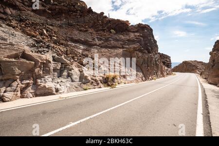 Rocky Road. Une route vide qui se courbe dans le désert rocheux de flanc de colline dans un paysage chaud et aride. Banque D'Images