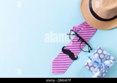 Concept de fête des pères heureux. Vue de dessus de cravate rose, magnifique boîte cadeau, chapeau, lunettes et moustache sur fond bleu vif pastel. Pose à plat. Banque D'Images