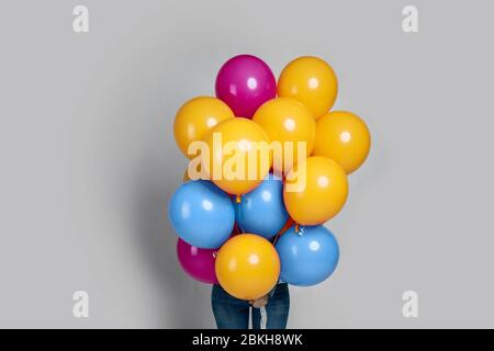 femme cachant son visage avec des ballons colorés sur fond gris. Banque D'Images