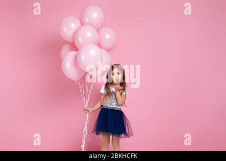 Une adorable petite fille souriante avec des ballons d'air rose pastel envoie un baiser isolé sur fond rose. Fête d'anniversaire. Espace de copie Banque D'Images