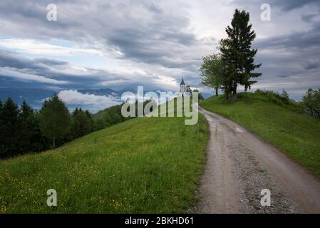 L'église Jamnik sur une colline au printemps, temps brumeux au coucher du soleil en Slovénie, Europe. Paysage de montagne peu après la pluie de printemps. Alpes slovènes. Banque D'Images