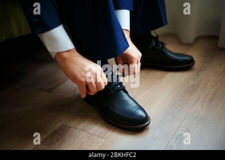Homme attachant les lacets sur des chaussures noires sur un parquet. Banque D'Images