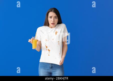 Jeune femme dans des vêtements sales buvant du jus sur fond de couleur Banque D'Images