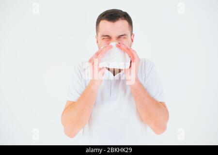 Jeune homme isolé sur fond blanc. Couvrir le nez avec un tissu blanc. Malade et malade éternuant dans une serviette blanche. Symptômes du coronairust. Banque D'Images