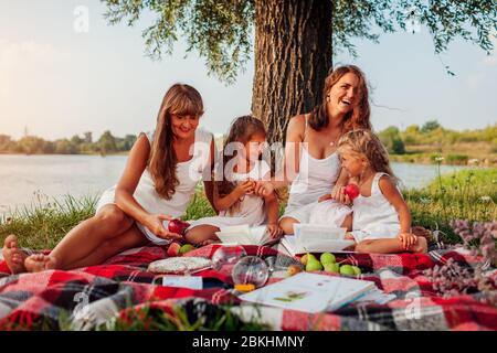 Fête des mères. Famille pique-nique au bord de la rivière Spring au coucher du soleil. Mère, grand-mère et enfants riant. Banque D'Images