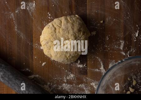 Vue de dessus de la pâte à scone au fromage enroulée en boule sur une surface en bois entourée de farine, d'une broche de roulement et d'un bol en verre transparent Banque D'Images