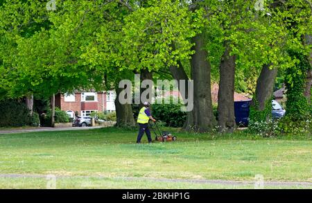 Un homme s'est engagé dans la coupe d'herbe sur un petit vert dans une zone résidentielle de Hellesdon, Norfolk, Angleterre, Royaume-Uni. Banque D'Images