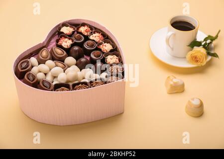 Boîte en forme de coeur avec bonbons au chocolat et tasse de café sur fond couleur Banque D'Images