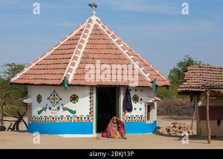 Inde, État du Gujarat, région de Kutch, village d'Adipur, ville de Bhuj à proximité, femme tribale de Meghwal portant des vêtements brodés traditionnels devant une hutte décorée de motifs colorés Banque D'Images