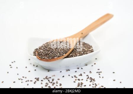 sur une surface blanche, renverser une grande quantité de graines de chia. Les petites graines sombres se dispersent autour du pot, créant une composition simple et minimaliste Banque D'Images