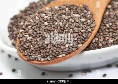 sur une surface blanche, renverser une grande quantité de graines de chia. Les petites graines sombres se dispersent autour du pot, créant une composition simple et minimaliste Banque D'Images