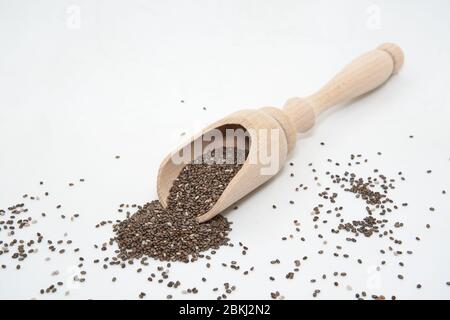sur une surface blanche, renverser une grande quantité de graines de chia. Les petites graines sombres se dispersent autour du pot, créant une composition simple et minimaliste Banque D'Images