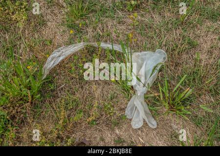 Un gant en latex de caoutchouc usagé jeté avec un morceau de plastique à côté de l'extérieur jeté dans la protection de l'herbe contre le coronavirus maintenant conta Banque D'Images