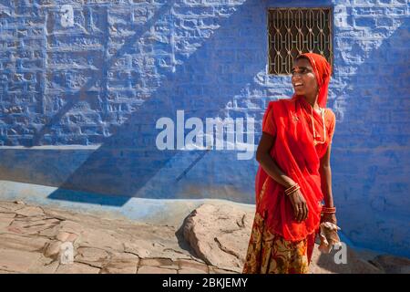 Inde, Rajasthan, Jodhpur, jeune femme en sari rouge marchant par une maison bleue Banque D'Images