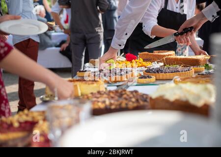 buffet de gâteaux avec des serveurs servant et des personnes esestivées prenant leurs parties à l'extérieur Banque D'Images