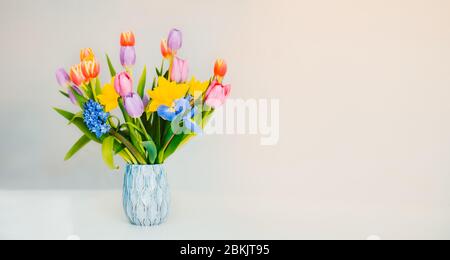 Printemps frais couleurs pastel bouquet de tulipes, jonquilles, iris dans vase debout sur une surface blanche avec fond beige clair. Fleurs festives pour gif Banque D'Images