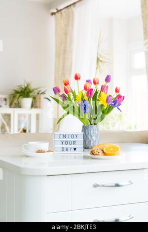 Concept Bonjour. Petit déjeuner romantique - fleurs fraîches, tasse de boisson chaude, petits gâteaux, orange, visionneuse avec message Profitez de votre journée sur une table en marbre avec Banque D'Images