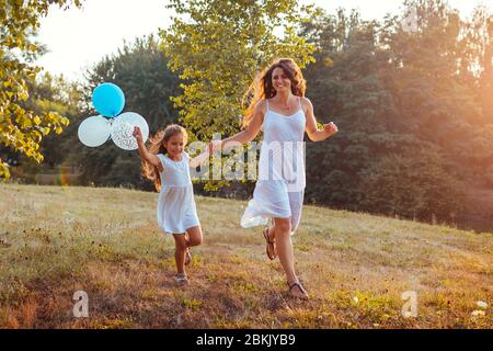 Fête des mères. Petite fille courir avec la mère et tenir des balons dans la main. Famille s'amuser dans le parc d'été Banque D'Images