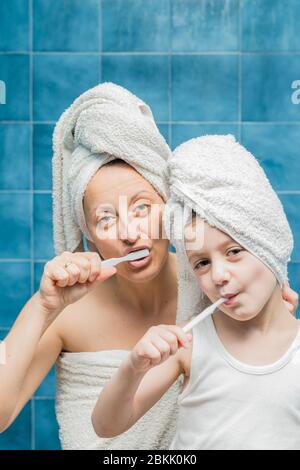 Une femme et un garçon avec des serviettes sur la tête se brossant les dents. Banque D'Images