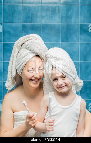 Une femme et un garçon avec des serviettes sur la tête se brossant les dents. Banque D'Images