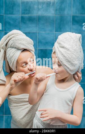 Une femme et un garçon avec des serviettes sur la tête se brossant les dents. Banque D'Images